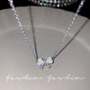 Silver crystal bow angel wings heart pendant necklace displayed on a white plate.