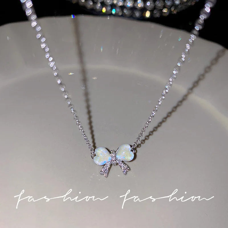 Silver crystal bow angel wings heart pendant necklace displayed on a white plate.