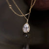 A close-up of a sterling silver water droplet pendant necklace featuring a clear zircon stone on a gold chain.