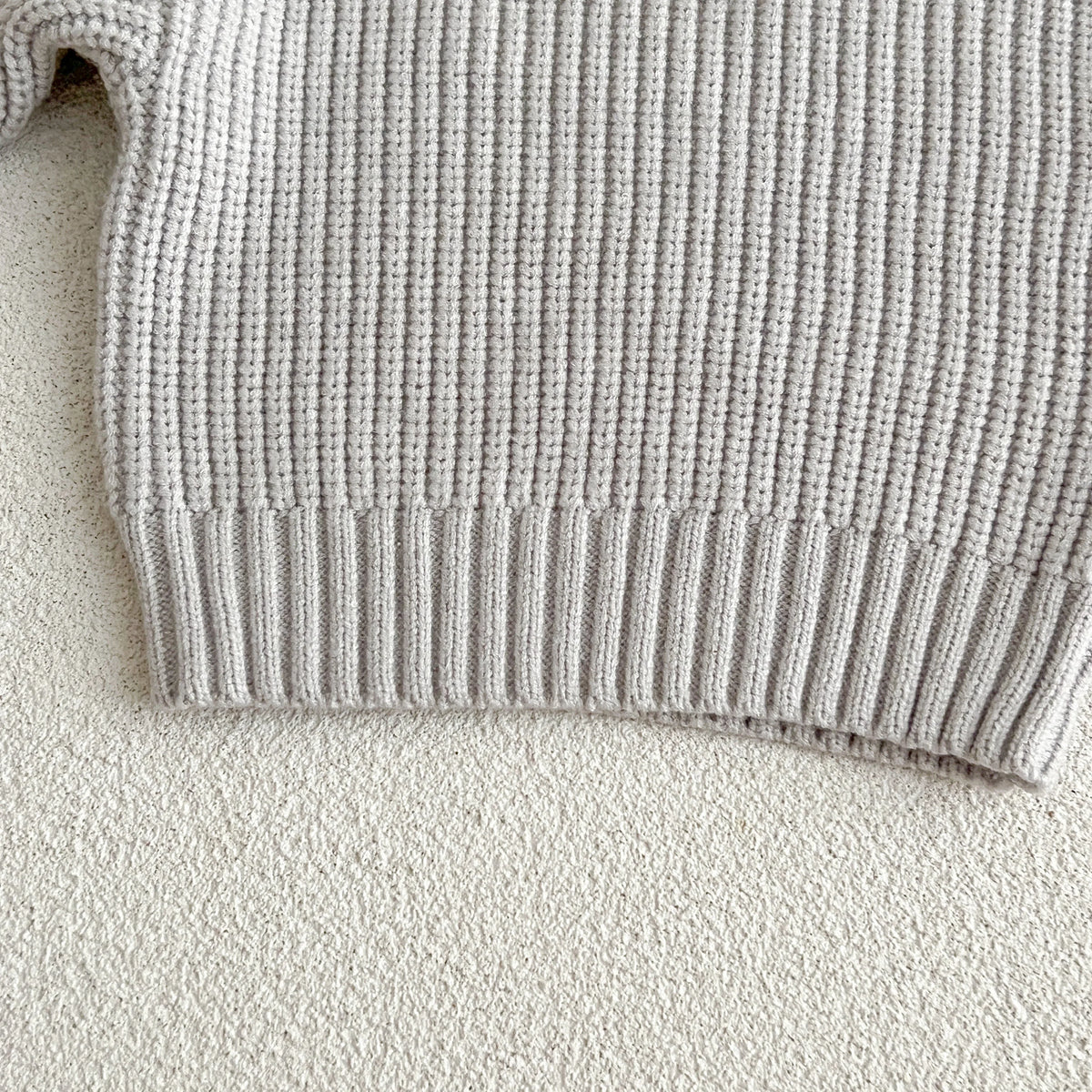 A light gray knit baby pullover sweater with a ribbed hem shown in close-up.