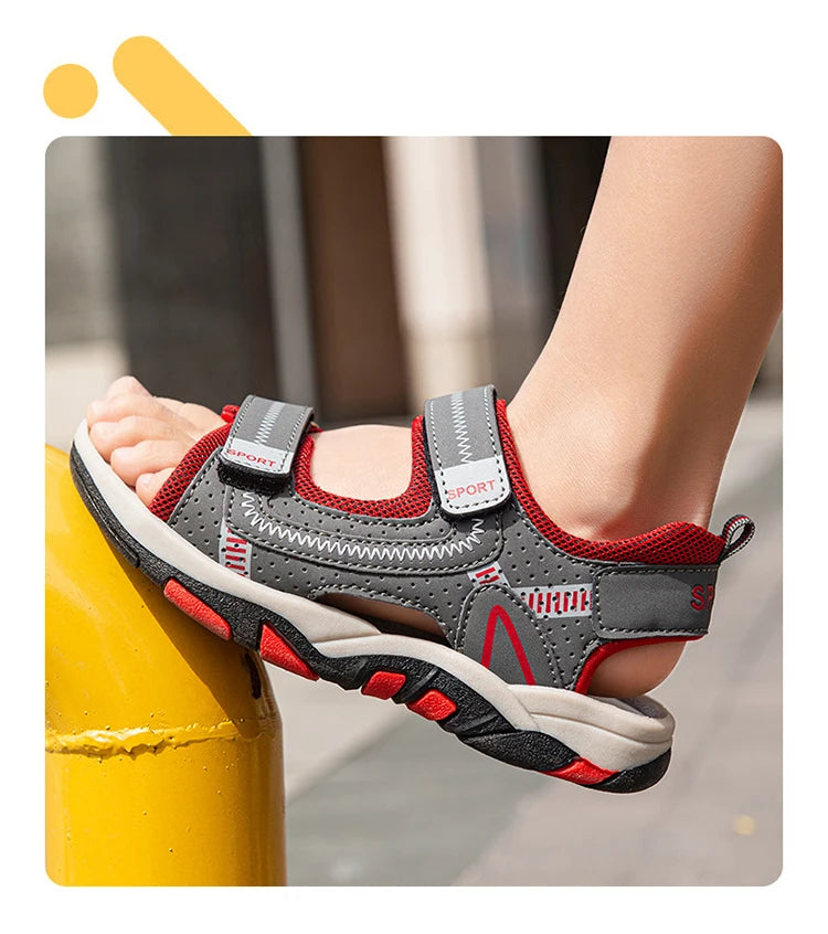 A close-up of a pair of gray and red boys' breathable summer sport sandals being worn on a foot.