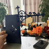 A black wrought iron shelf lamp with a decorative scroll design is displayed on a table.