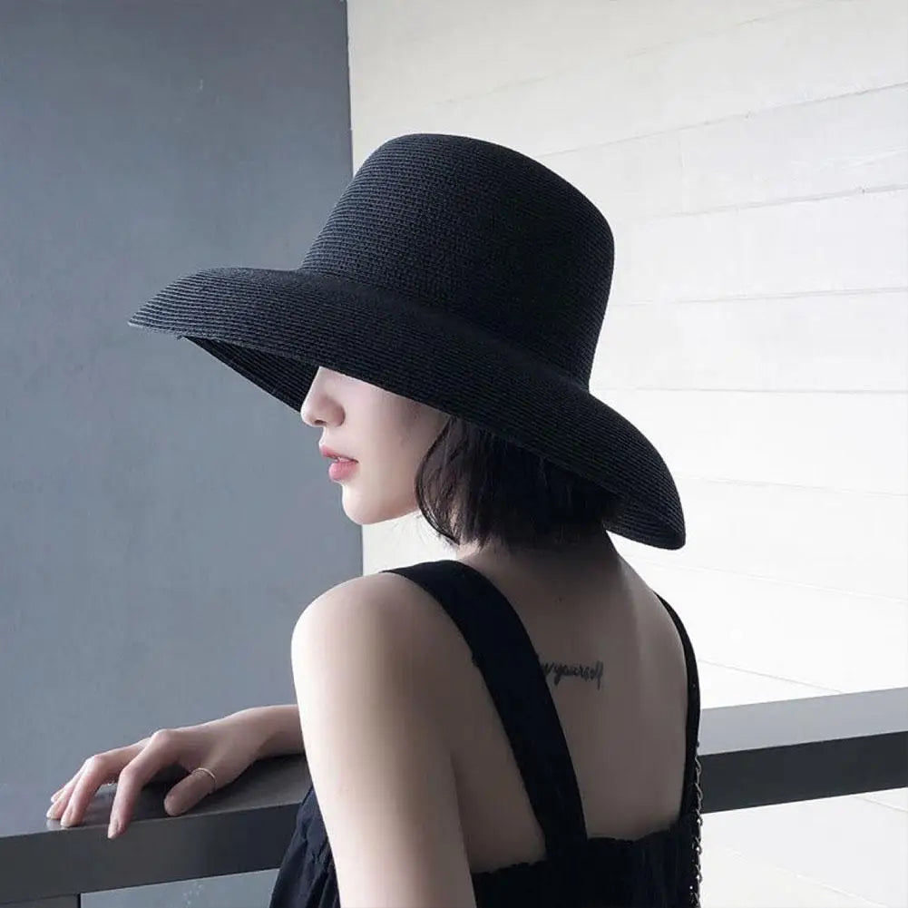 A woman wearing an elegant black wide brim straw sun hat, shown in profile against a light background.