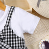 White t-shirt and black plaid overalls displayed next to a cream knit blanket.