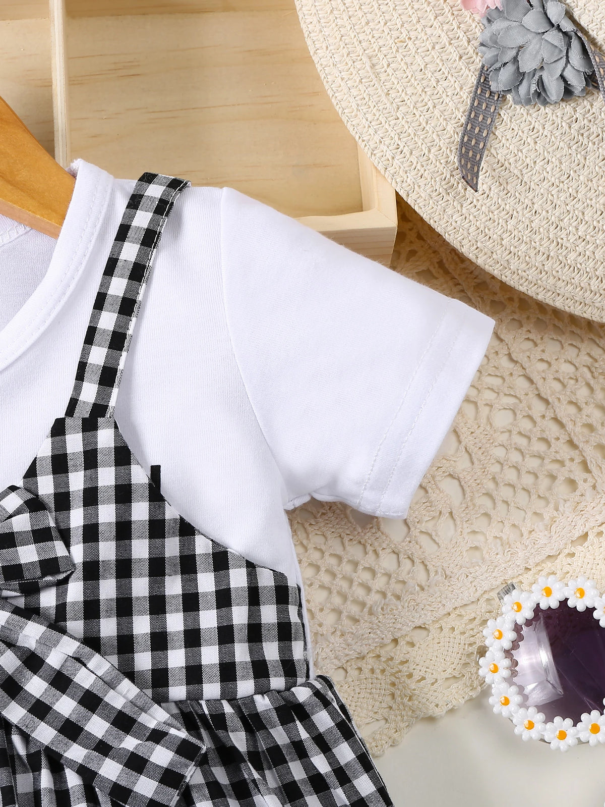 White t-shirt and black plaid overalls displayed next to a cream knit blanket.