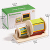 A wooden rolling drum toy with colorful dowels and a viewing window, packaged in a green box.