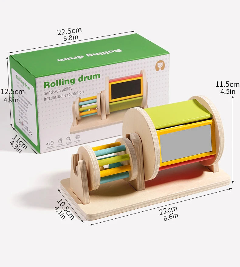 A wooden rolling drum toy with colorful dowels and a viewing window, packaged in a green box.