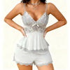 A woman models a light gray silky two-piece lounge set with a spaghetti strap top and matching shorts.