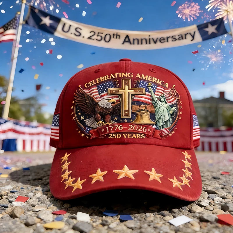A red baseball cap featuring a patriotic graphic design with an eagle, cross, and liberty statue, set against a blue sky.