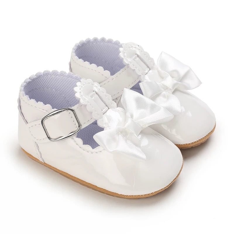 A pair of white baby first walker shoes with lace-up straps and ribbon bows