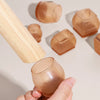A hand holds a silicone furniture leg pad with a felt bottom, showing various shapes and textures.