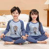 A boy and a girl wearing matching blue cotton astronaut pajama sets sitting on a bed.