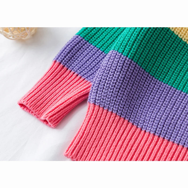 A close-up of a girls' rainbow striped knit sweater featuring vibrant pink, purple, and green horizontal stripes.
