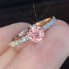 Nærbilde av en klassisk rund forlovelsesring i kubisk zirkonia med rosa midtstein og pavé-satt diamantbånd på en finger.