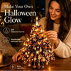 Kvinne pynter et DIY Halloween-glow-tre-sett med LED-lys på et trebord.
