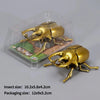 A golden wind-up insect toy, resembling a beetle or bee, is shown inside clear plastic packaging.