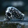 A silver gothic carved skull ring in 316L stainless steel resting on a dark stone surface.