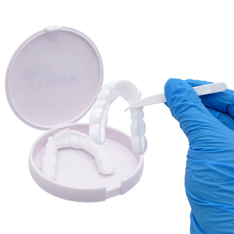 A hand in a blue glove holds a white cosmetic denture teeth kit with an acrylic model and a white tooth mold.