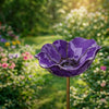 A handcrafted metal purple flower garden stake shaped like a bowl or bird bath, set in a lush green garden.