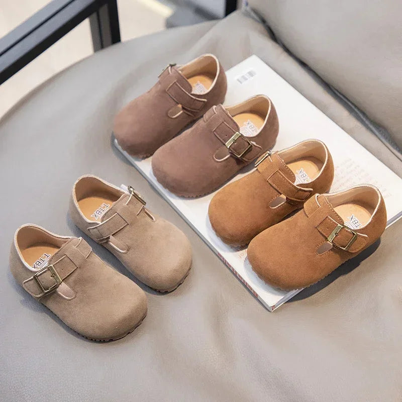 A collection of tan suede non-slip kids' moccasin shoes with hook-and-loop closures displayed on a light gray surface.