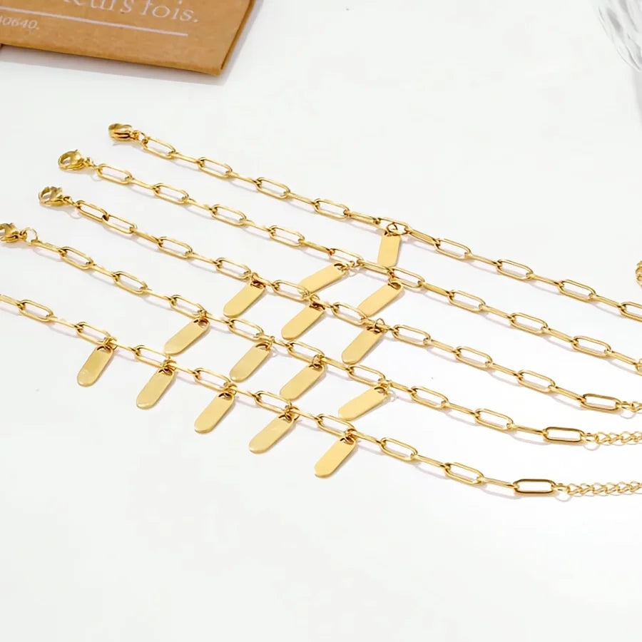 Varios brazaletes de acero inoxidable bañados en oro con cadenas ajustables sobre una superficie blanca.