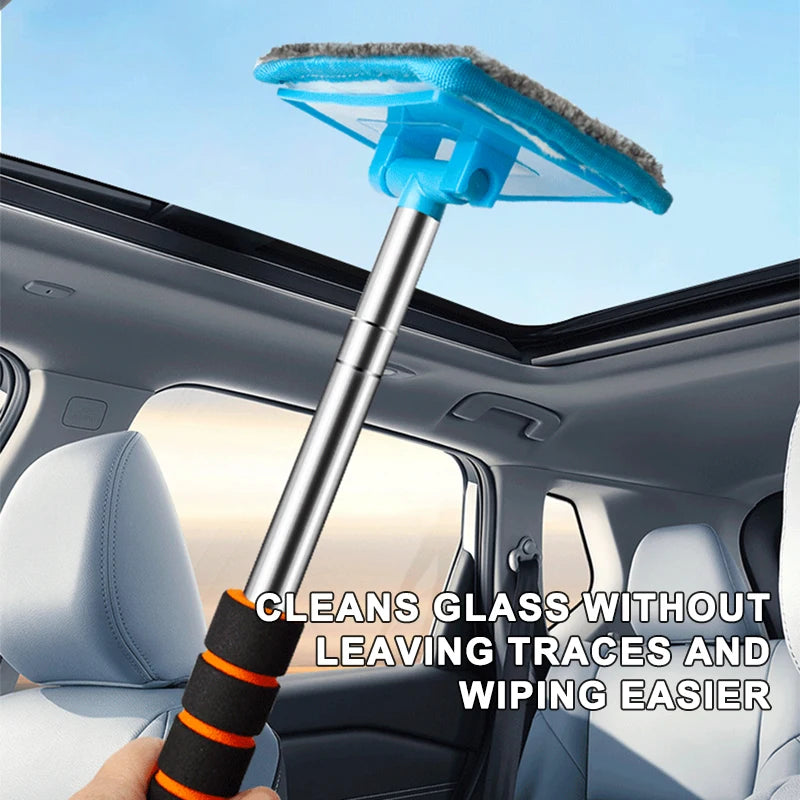 A hand holds a telescopic windshield cleaning brush with a blue, fuzzy head inside a car cabin.