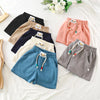 A collection of kids beach shorts in various pastel and earth tones laid out on a white surface.