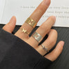 A hand displays a set of gold rings featuring vintage geometric, cross, pearl, and butterfly designs.
