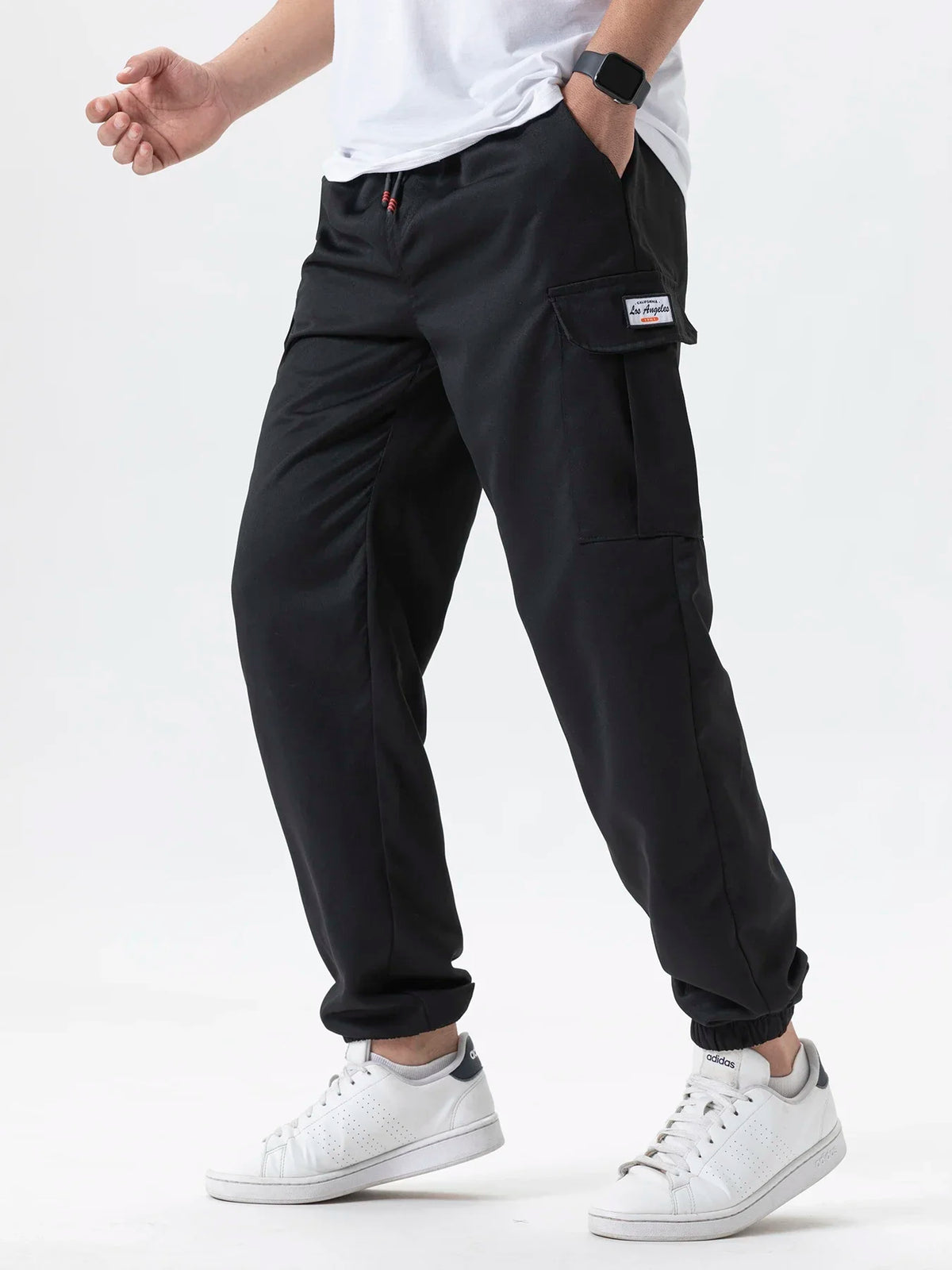 A man wearing black cargo joggers and a white shirt standing, showing the fit of the pants.
