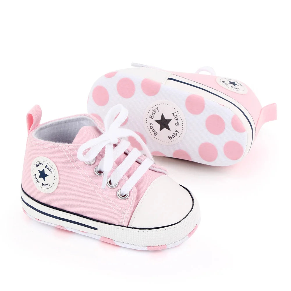 Pink canvas baby sneakers with white laces and a non-slip sole, shown next to the shoe box.