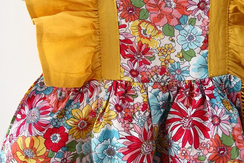 A close-up of a baby girl's floral print dress featuring yellow puff sleeves and a matching hat.