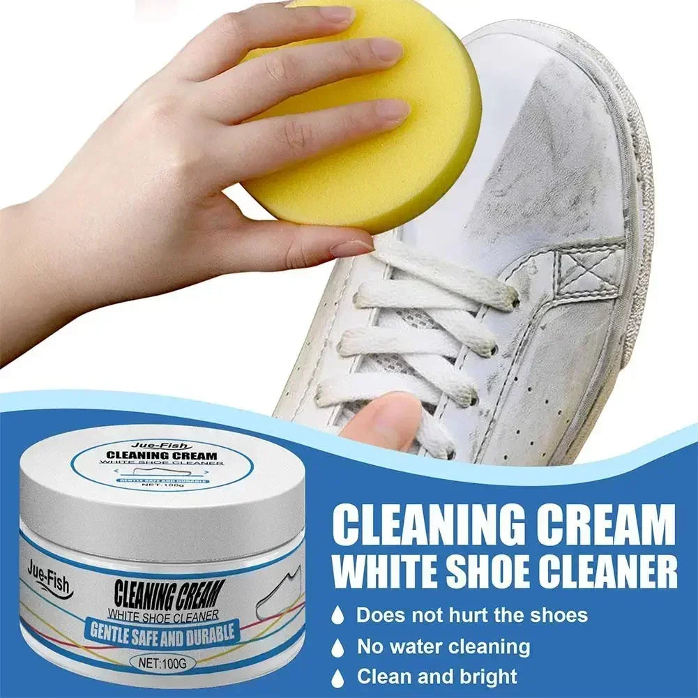 A hand holds a yellow cleaning cream sponge next to a white shoe cleaner jar and a white sneaker.
