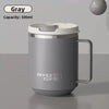 A gray double wall insulated stainless steel travel mug with a silver lid and handle sitting on a surface.