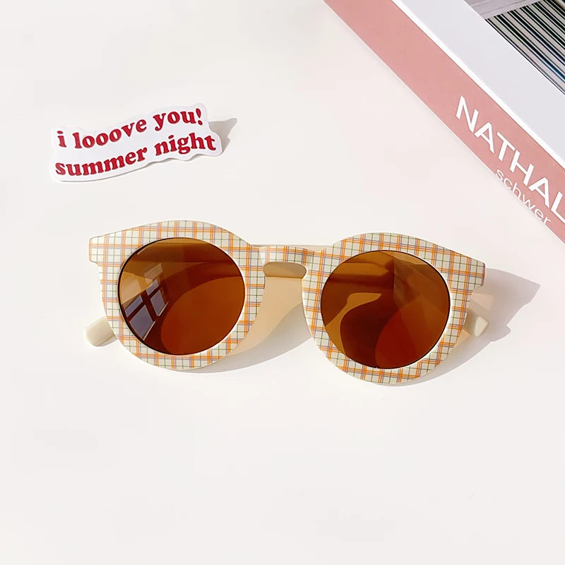 A pair of kids polarized sunglasses with an orange-tinted lens and a light yellow plaid frame resting on a white surface.