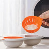 Cuiseur d'œufs en silicone orange utilisé au micro-ondes, avec deux bols blancs assortis.
