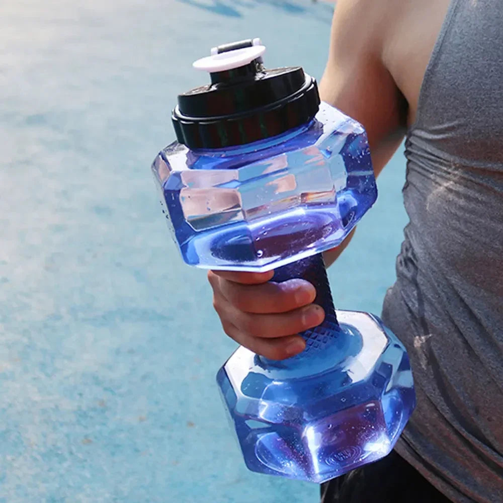 Mano sostiene una botella de agua deportiva azul transparente con forma de pesa y tapa negra segura.
