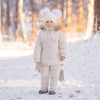 A child wearing a beige winter down jacket and pants set with a faux fur hood standing in the snow.