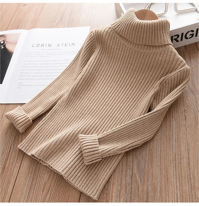A beige knit turtleneck sweater for kids displayed on a wooden surface.