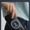 En hånd legger et svart, sammenleggbart magnetisk telefonringstativ i lommen på mørkeblå jeans.