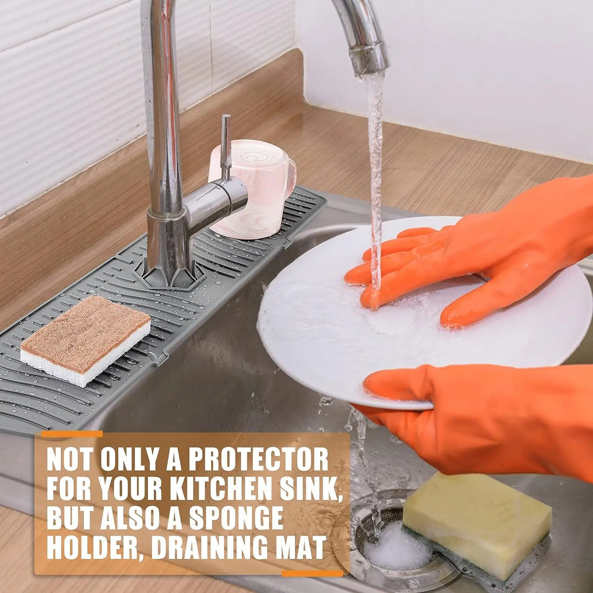 An orange gloved hand is pouring water from a kitchen sink faucet onto a white sponge holder draining mat.