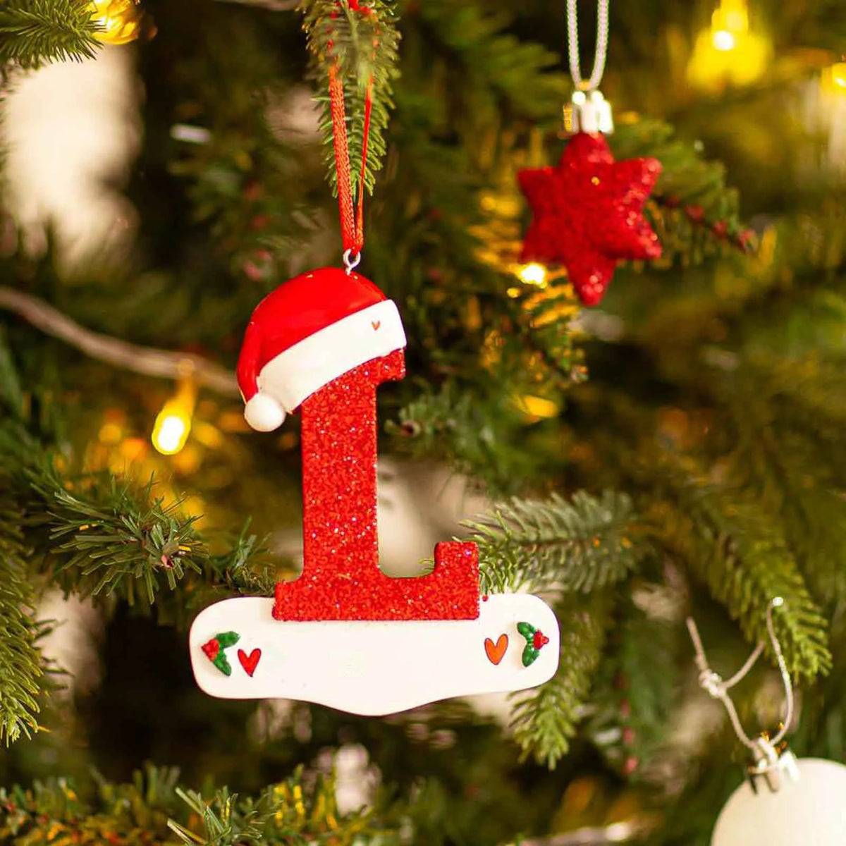Rød glitter-akryl nummer én-ornament hengende på en grønn juletregren.