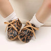 Pair of leopard print baby first walkers with soft rubber soles shown on a person's foot.