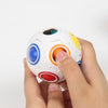 A hand is holding a white rainbow fidget cube with colorful gems, demonstrating its use for stress relief.