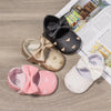A set of three baby shoes with bow knots and heart designs in black, gold, and pink.