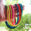 A hand holds a bundle of rainbow colored elastic jump ropes, including red, orange, yellow, green, and blue.