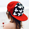 A close-up shot of a red baseball cap with a black and white Mickey Mouse print, worn by a person outdoors.