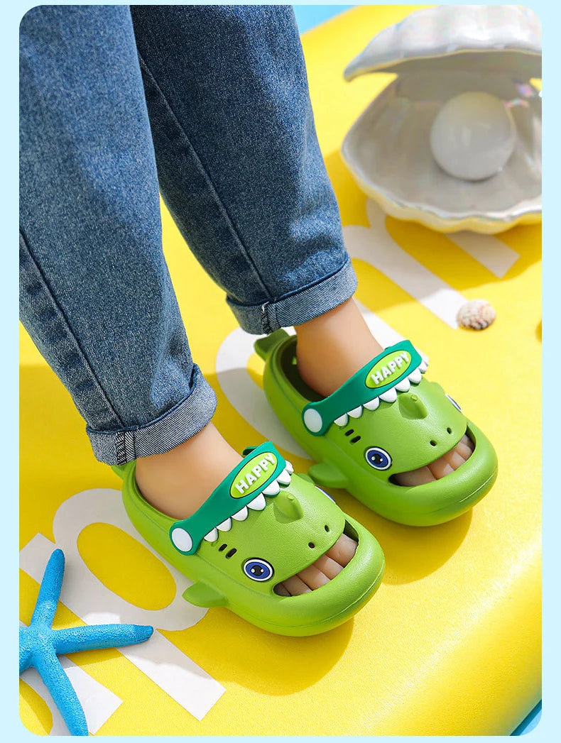A pair of bright green kids shark clog sandals with anti-slip soles resting on a yellow surface.