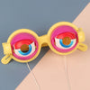 A pair of novelty funny glasses with bright yellow frames and pink lenses resting on a light background.