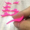 A hand holds a set of pink winged eyeliner stencils on a light wooden surface.