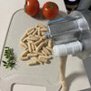A silver pasta maker machine is shown next to fresh tomatoes and a pile of dry cavatelli pasta.